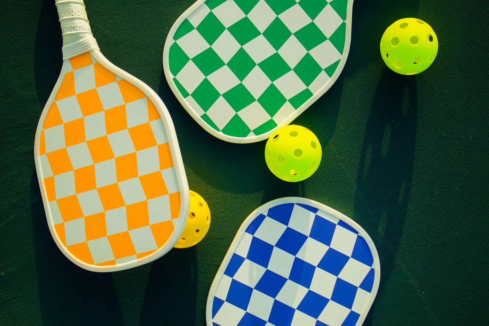 Checkered pickleball paddles and bright balls laid out on a court